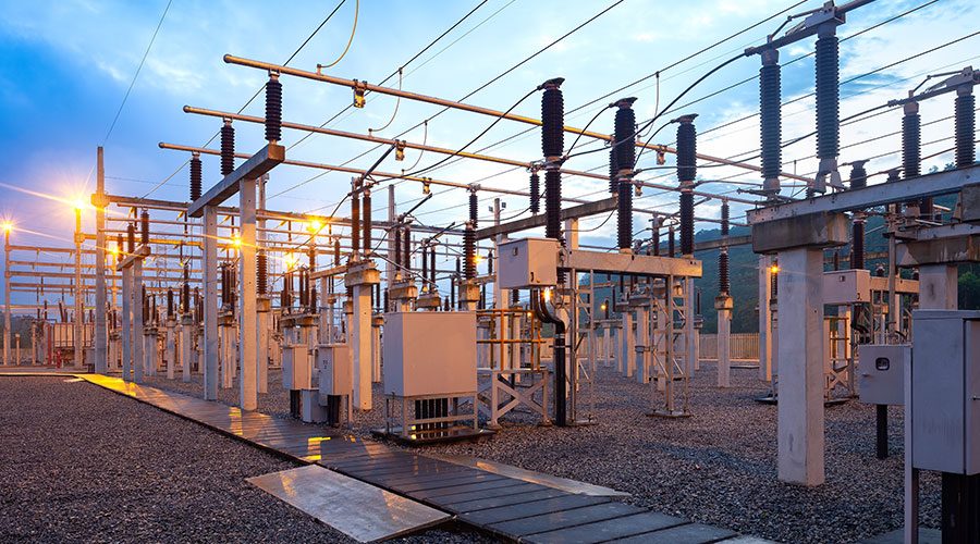 High voltage switchgear, disconnects and insulators standing in an outdoor industrial substation yard at dusk.